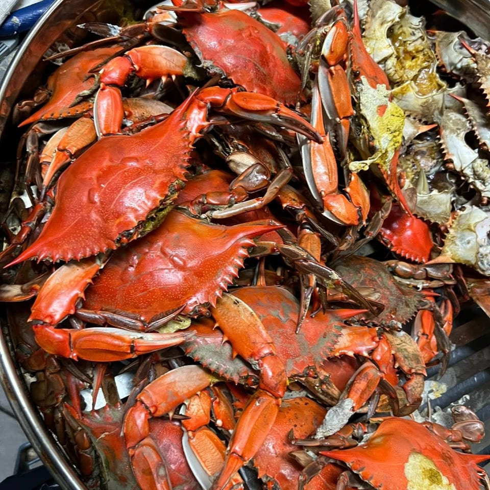 A large pot filled with many bright red, cooked Cajun crabs, some with shells removed.