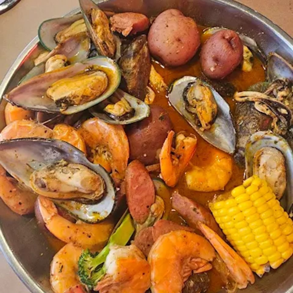 Cajun seafood boil with mussels, shrimp, potatoes, sausage, corn, and broccoli in a metal bowl.