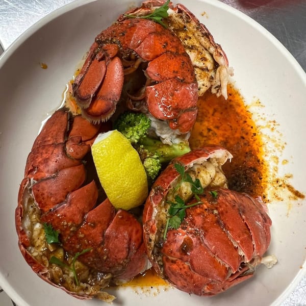 Cajun Crab's grilled lobster tails with broccoli, lemon, and spicy sauce in a white bowl.
